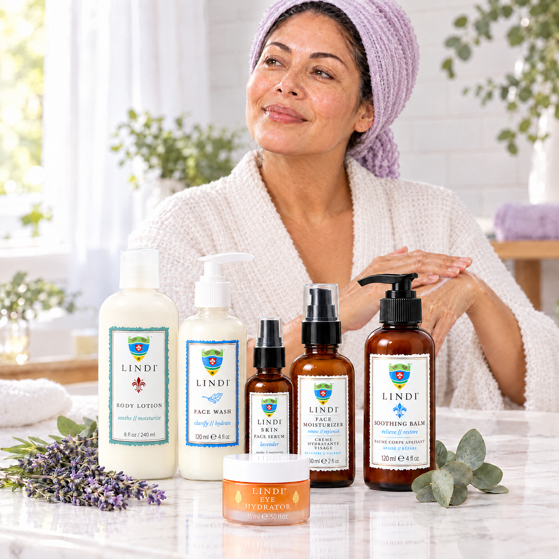 Woman in a head wrap smoothing on Lindi Skin lotion, with Lindi Skin Body Lotion, Face Wash, Face Serum, Face Moisturizer, Soothing Balm and Eye Hydrator in front
